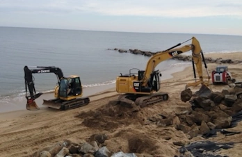 Excavators operating on a sandy beach shoreline next to the ocean.