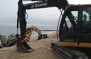 View from behind a Deere excavator looking out over a beach construction site.