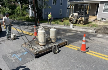 Paving crew using an infrared asphalt heater for seamless pavement repair on a street in Ayer, MA