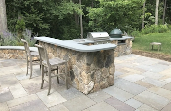 Masonry outdoor kitchen featuring a brick smoker and bar seating in Concord, Massachusetts