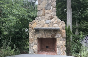 Backyard outdoor kitchen with brick fireplace, smoker, and entertaining area in Concord, Massachusetts