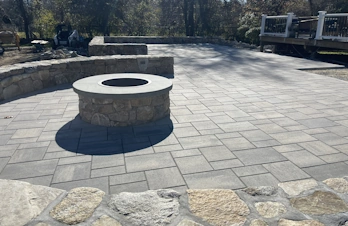 Holliston, Massachusetts commercial patio at Twisted Carrot featuring light gray pavers, fieldstone retaining walls, and a circular stone fire pit.