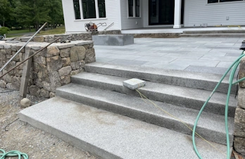 Wide natural stone patio steps connecting multiple outdoor living areas in Concord, Massachusetts