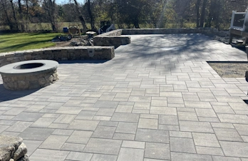 Large paver patio with a circular fire pit and outdoor seating in Holliston, Massachusetts