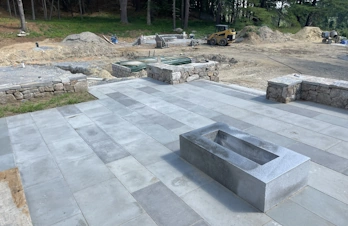 Concord, Massachusetts bluestone patio featuring a sleek rectangular stone fire pit, fieldstone retaining walls, and stone seating.