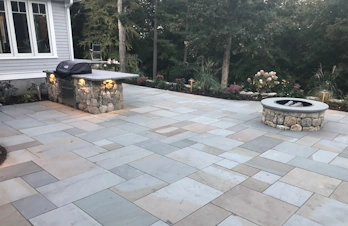 Concord, Massachusetts residential bluestone patio featuring a built-in stone grill island and circular fieldstone fire pit.