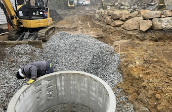 A worker inspecting a round concrete drainage riser set in crushed stone.
