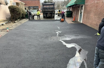 Freshly paved asphalt alley with a storm drain grate and sealed surface lines.