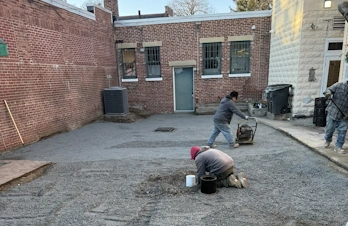 Workers operating in a paved court area framed by brick buildings.